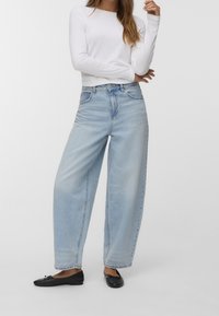 Světle modré široké džíny vyrobené z denimu, s vysokým pasem, mají pět kapsiček a kontrastní stehy, v kombinaci s černými balerínami.