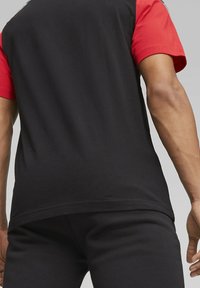 Camiseta atlética de manga corta en negro y rojo, fabricada con un tejido transpirable; presenta un diseño de mangas en color contrastante y un corte ajustado.