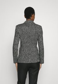 Op maat gemaakte zwart-wit getextureerde blazer met een kraag met inkeping, sluiting met één knoop en een aansluitende silhouet, gecombineerd met zwarte broek.