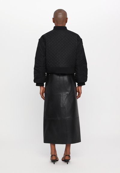 Giacca bomber nera trapuntata con un design corto, abbinata a una gonna maxi in pelle nera, con una texture liscia e cuciture sottili.