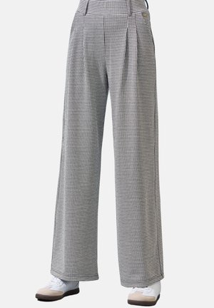 High-waisted, wide-leg trousers with black and white houndstooth pattern worn with white and beige sneakers.