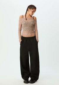 Lys pink, tekstureret langærmet top med off-shoulder design, parret med brede sorte bukser og klodsede sorte sko.