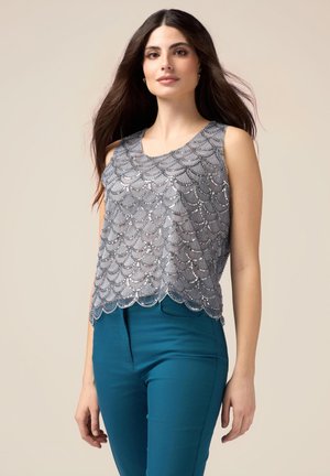 Top argento senza maniche con design a scallop e decorazioni in paillettes, abbinato a pantaloni aderenti color teal. Tessuto liscio, silhouette moderna.
