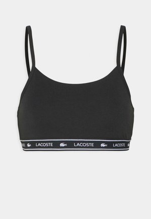 Juoda sportinė liemenėlė plonais dirželiais, pagaminta iš lygaus audinio. Savybė - prekės ženklu pažymėtas elastingas diržas su "LACOSTE" tekstu ir balta logo.