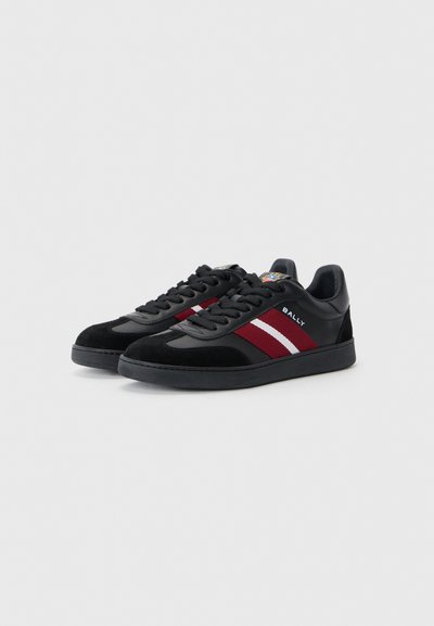 Sneakers neri realizzati in materiali scamosciati e in pelle, con strisce rosse e bianche, suola piatta e design con lacci. Logo del marchio in evidenza.