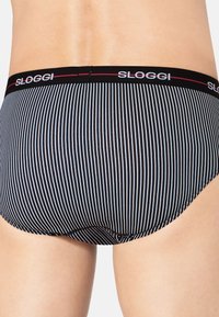 Schwarz-weiße gestreifte SLOGGI Slips mit enganliegendem Schnitt und weichem Bund mit Logo. Glatte Textur ohne sichtbare Nähte.