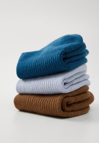 Drei Paar Socken gestapelt: oben in Blau, in der Mitte in Hellgrau, unten in Braun. Alle haben eine gerippte Struktur und einen weichen Stoff.