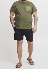 Oliven grøn bomulds t-shirt med en brystlomme, kombineret med sorte bomulds shorts og brune sandaler. Afslappet, løs pasform.