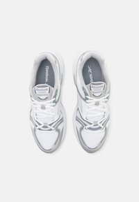 Tênis atléticos brancos com detalhes em cinza, parte superior em malha, sola acolchoada e fechamento com cadarços, exibindo o logotipo da Reebok na língua e na palmilha.
