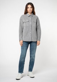 Grijze corduroy overhemdjack met een kraag, twee voorkruiken, knoopsluiting en lange mouwen, gecombineerd met blauwe spijkerbroek en witte sneakers.