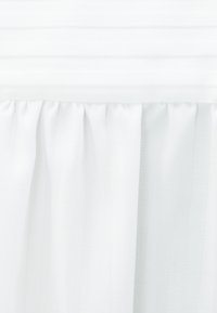 Panneau de rideau blanc transparent avec le haut froncé suspendu sur un fond en bois blanc.