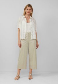 Chemise blanche en voile avec un motif de vagues sur un débardeur blanc, associée à un pantalon large beige et des sandales beiges avec des détails de sangles.