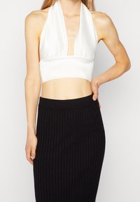 Weißes Satin-Haltertop mit tiefem V-Ausschnitt und gerafftem Detail an der Taille, kombiniert mit einem schwarzen gerippten Strickrock.
