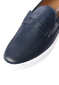 Mocassini in pelle blu scuro con un design cucito, dotati di una suola in gomma bianca e una fascia decorativa davanti.