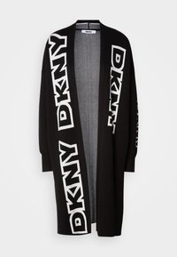 Dolg črn kardigan s širokimi rokavi, ki ima izrazite bele DKNY logotipe vzdolž spredaj in na rokavih. Mehak, teksturiran material.