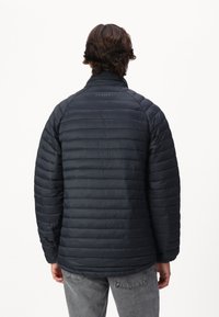 Izolowana, ciemnoniebieska kurtka puchowa o pikowanej fakturze, z wysokim kołnierzem i detalem z logo. Posiada długie rękawy i luźny krój.