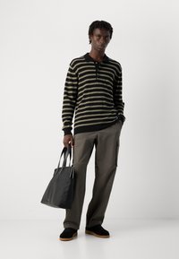 Stripet, langermet polo i svart og olivengrønn med krage, kombinert med olivengrønne cargo-bukser og en svart totebag. Svart sneakers.