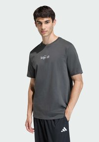 Šedé tričko s kulatým výstřihem vyrobené z bavlny, s malým bílým logem "Stripe Café" na hrudi, spárované s černými tepláky.