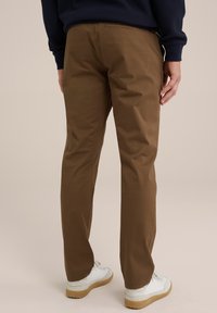 Braune Baumwollhosen mit geradem Schnitt, ausgestattet mit Gesäßtaschen, kombiniert mit weißen Sneakers und einem strukturierten blauen Oberteil.