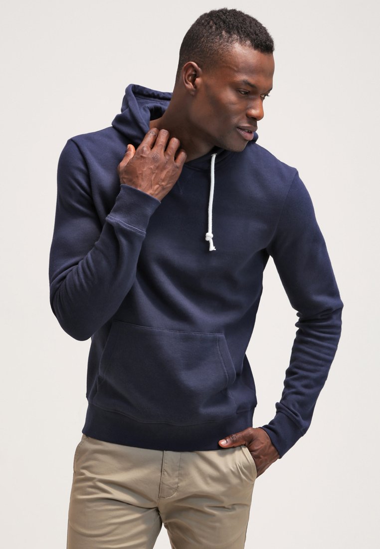 Navy blue hoodie made of soft fabric, featuring a kangaroo pocket, drawstring hood, and ribbed cuffs. Model has a neutral pose.