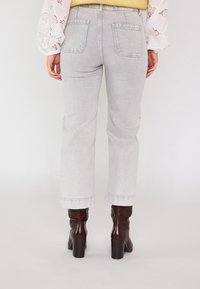 Jeans grigi alti in vita con taglio dritto, orlo sfrangiato e tasche posteriori, abbinati a stivali con tacco lucidi di colore marrone.