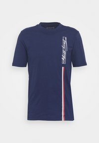 Marinblå bomulls t-shirt med kort ärm, rund hals, vitt grafiskt detalj på vänster sida och röda och vita vertikala ränder.