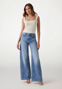 Débardeur en tricot beige clair associé à un jean large en denim bleu clair. Le jean présente une finition délavée et une taille haute.