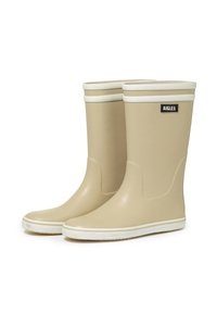 Bottes de pluie en caoutchouc beige avec des accents blancs en haut et à la semelle, présentant un design incurvé et un petit patch logo noir.