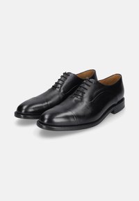 Ein Paar schwarze, polierte Lederanzugschuhe mit geschlossener Schnürung und niedrigem Absatz auf einem weißen Hintergrund.