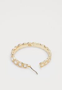 Anello d'oro con bordi lisci e ondulati alternati, dotato di pietre trasparenti incastonate in cornici circolari lungo un lato. Incluso un dettaglio in metallo.