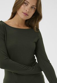 Langærmet, figursyet top i mørkegrønt stof. Har en bred halsudskæring og en glat tekstur, hvilket fremhæver et enkelt og elegant design.