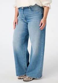 Lichtblauwe wijdlopende jeans hebben een hoge taille, rechte snit en subtiele vervaging. Gecombineerd met gestructureerde schoenen met een patroon.