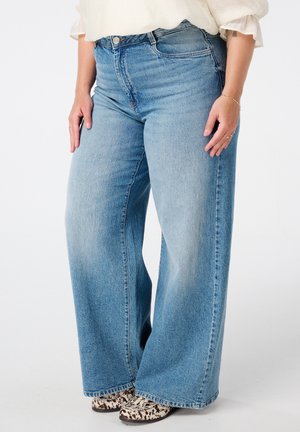 Lichtblauwe wijdlopende jeans hebben een hoge taille, rechte snit en subtiele vervaging. Gecombineerd met gestructureerde schoenen met een patroon.