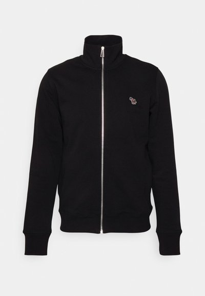 Veste noire zippée avec col montant, en tissu doux. Présente des poignets et un ourlet côtelés, ainsi qu'un petit détail brodé sur la poitrine.