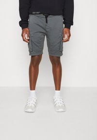 Shorts cargo gris avec poches latérales, taille à cordon de serrage et en mélange de coton. Portés avec des sneakers blanches et des chaussettes à mi-mollet.