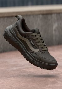 Dark olive green sneaker with a textured mesh upper, padded collar, and a rugged sole. Features tonal accents and flat laces.