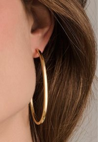 Guldörhänge, cirkelär form, polerad yta, medeltjocklek, placerad genom örsnibben, med brunt hår i bakgrunden.