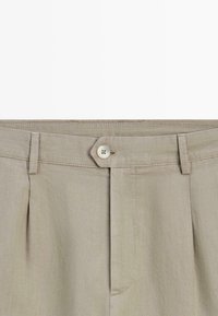 Beige byxor med hög midja, knäppt midjeband, bältesöglor och främre veck.