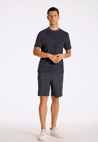 Granatowa koszulka z krótkim rękawem o fakturowanym wykończeniu, w połączeniu z pasującymi szortami. Posiada okrągły dekolt, lekką tkaninę i białe trampki.