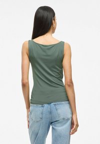 Haut sans manches vert olive avec un col bateau, en tissu lisse, associé à un jean taille haute bleu clair.