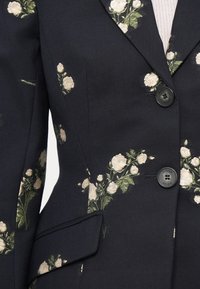 Granatowa marynarka z białym haftem kwiatowym, podwójnym zapięciem na guziki oraz klapami. Teksturowany materiał z bocznymi kieszeniami.