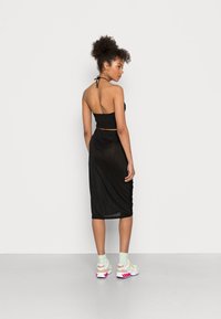 Vestido halter preto com um design ajustado que cai abaixo do joelho, combinado com ténis brancos destacados com detalhes em rosa e amarelo.