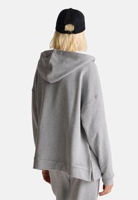 Felpa grigia oversize con cappuccio regolabile, polsini a coste e spacchi laterali. Tessuto testurizzato con un logo discreto sull'orlo. Cappellino nero.