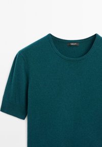 Türkises Strickoberteil mit kurzen Ärmeln, das einen runden Ausschnitt und eine weiche Textur aufweist. Etikett im Nackenbereich sichtbar; schlichtes Design und nahtloser Abschluss.