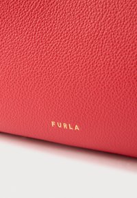 Κόκκινη τσάντα από δέρμα με υφή και εμφανές χρυσό λογότυπο «Furla». Η επιφάνεια παρουσιάζει λεπτό κόκκο, προσδίδοντας μια κομψή εμφάνιση.
