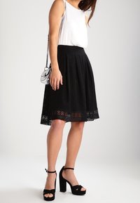 Sort plisseret nederdel med blondekant, kombineret med en tætsiddende hvid top. Sorte plateauhæle fremhæver looket. Sølv crossbody-taske inkluderet.