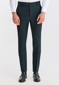 Ciemnozielone, dopasowane spodnie z płaskim przodem, o wąskim kroju i gładkiej fakturze. W zestawieniu z czarnymi mokasynami, podkreślającymi formalny wygląd.