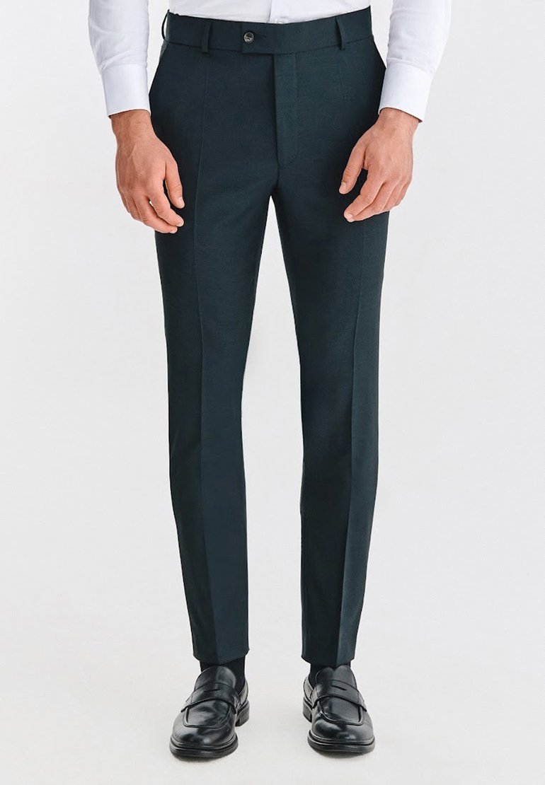 Ciemnozielone, dopasowane spodnie z płaskim przodem, o wąskim kroju i gładkiej fakturze. W zestawieniu z czarnymi mokasynami, podkreślającymi formalny wygląd.