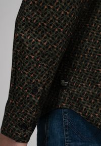 Langermig shirt in zwart met een geometrisch patroon in groen en koraal. Voorzien van knoopmanchetten en een merklabel aan de zoom.