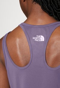 Fioletowy top na ramiączkach z okrągłym dekoltem i designem w stylu wyścigowym. Posiada biały logotyp na plecach oraz gładką teksturę materiału.